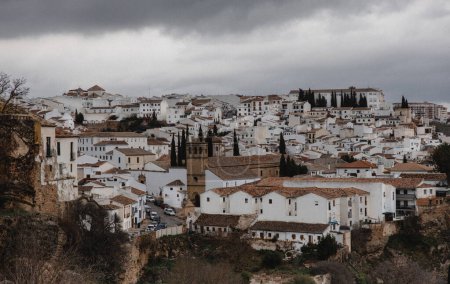Foto de "Cielos nublados se ciernen sobre las tradicionales casas blancas y la arquitectura histórica de Ronda, España, enclavada en una ladera." - Imagen libre de derechos