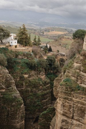 Foto de "Pintoresco paisaje de Ronda, con el famoso Puente Nuevo sobre el desfiladero de El Tajo, rodeado de exuberante vegetación y edificios históricos." - Imagen libre de derechos