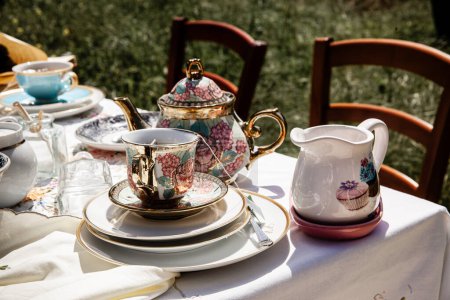 "Experimente la elegancia de una hora clásica del té con esta exquisita tetera floral y taza a juego, colocada en una mesa iluminada por el sol con encanto pastoral."