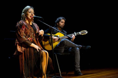 Téléchargez les photos : "Chanteuse de flamenco avec microphone et guitariste, baignée d'éclairage scénique." - en image libre de droit