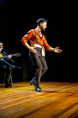 Téléchargez les photos : Un danseur solo de flamenco masculin montre ses talents sur scène avec un guitariste accompagnant en douceur. Photo verticale - en image libre de droit