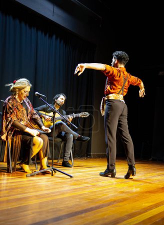 Téléchargez les photos : Danseuse de flamenco masculine commandant la scène avec une posture expressive tandis que les musiciens assis fournissent le rythme, photo verticale. - en image libre de droit