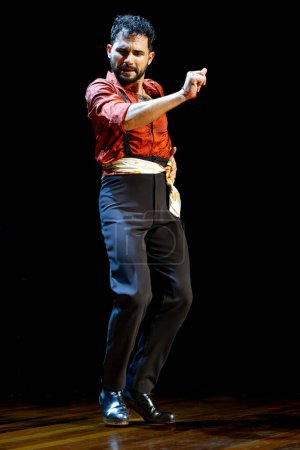 Foto de Bailarina flamenca masculina con una expresión enfocada y un gesto dinámico que se realiza bajo el foco del escenario, foto vertical. - Imagen libre de derechos