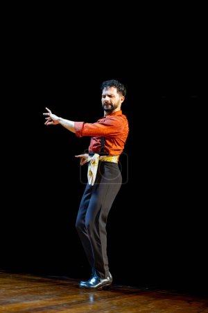 Foto de Un bailaor flamenco masculino con gestos expresivos en la mano actúa en el escenario, vestido con una camisa roja ricamente tonificada. - Imagen libre de derechos