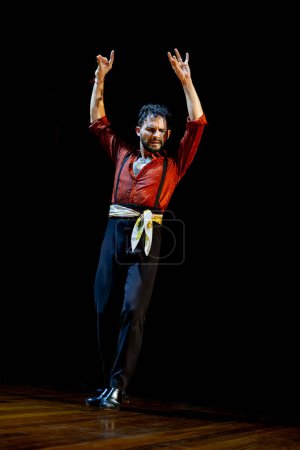 Téléchargez les photos : Un danseur de flamenco masculin émotif lève les bras dans une posture de danse traditionnelle sur une scène éclairée. - en image libre de droit