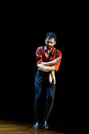 Photo for Male flamenco dancer expresses deep emotion through his pose on a dark stage, wearing a vivid red shirt, vertical photo. - Royalty Free Image