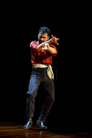 Foto de Bailarina flamenca masculina con camisa roja capta la intensidad del baile con potentes movimientos de brazos en el escenario. - Imagen libre de derechos
