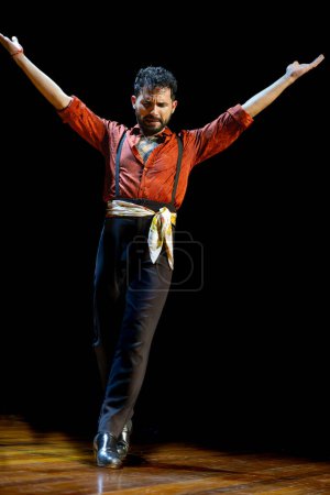 Photo for A male flamenco dancer opens his arms wide, channeling the intensity of the performance on a dark stage, vertical photo. - Royalty Free Image