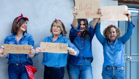 Foto de Un alegre grupo de mujeres en ropa de mezclilla, orgullosamente sosteniendo mensajes de empoderamiento, irradiando unidad y fuerza femenina. - Imagen libre de derechos