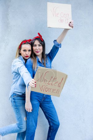 Two women stand close, confidently holding signs that read 'United Women' and 'We can do it', embodying the spirit of female solidarity and empowerment."