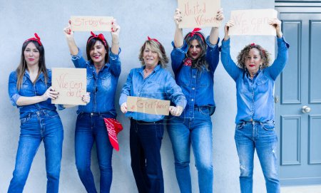 Téléchargez les photos : "Les femmes en denim avec des bandanas rouges soulèvent des signes avec des messages d'autonomisation des femmes, célébrant l'amitié et le courage." - en image libre de droit