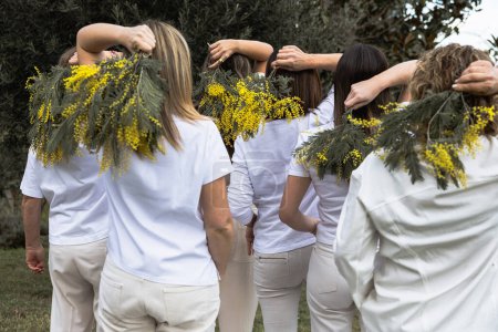 A back view of women in white shirts united with yellow mimosa bouquets, symbolizing support and empowerment on Women's Day.