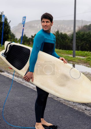 Téléchargez les photos : Un surfeur portant sa planche de surf, se dirigeant avec impatience vers la plage pour une session. - en image libre de droit