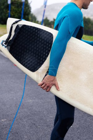 Téléchargez les photos : Vue latérale d'un surfeur en combinaison portant sa planche de surf, prêt à attraper les vagues. - en image libre de droit