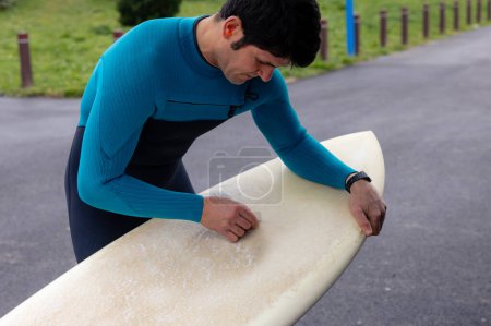 Foto de Surfista aplicando cera a su tabla de surf para una tracción óptima. - Imagen libre de derechos
