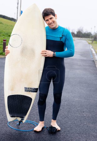 Foto de Un joven surfista sonriente con su tabla, listo para el mar. - Imagen libre de derechos
