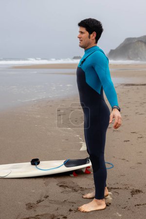 Foto de Feliz surfista en la orilla mirando al mar y estirándose antes de entrar en el agua - Imagen libre de derechos
