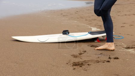 Photo for Cut out of a surfer's legs on the beach with a surfboard. - Royalty Free Image