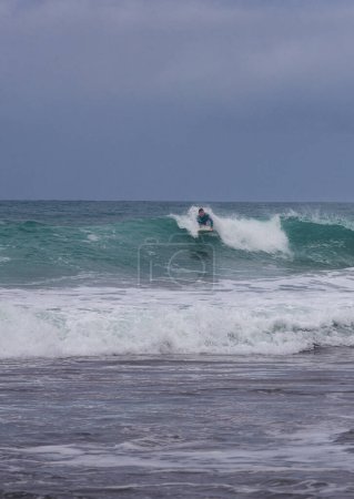 Téléchargez les photos : Plan d'action d'un surfeur en combinaison bleue surfant habilement sur une vague lors d'une journée sombre à la plage. - en image libre de droit