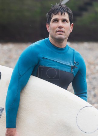Ein Surfer blickt nachdenklich in die Ferne, das Brett in der Hand, am Meer, nachdem er auf den Wellen geritten ist.