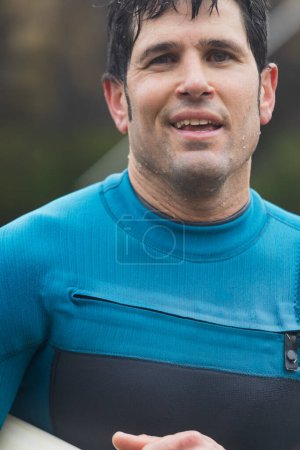 Portrait of a smiling surfer, content after an enjoyable surf session, with his board and wearing a wetsuit.