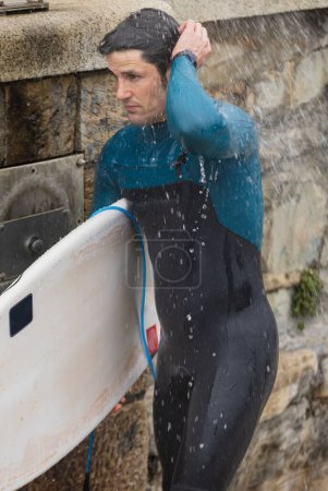 Un surfeur se rince sous une douche au bord de la plage, nettoyant après une journée de balade sur les vagues.