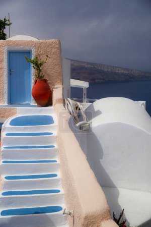 Téléchargez les photos : La charmante porte bleue et les marches traditionnelles des Cyclades mènent à une vue imprenable sur la mer Égée à Santorin, en Grèce. - en image libre de droit