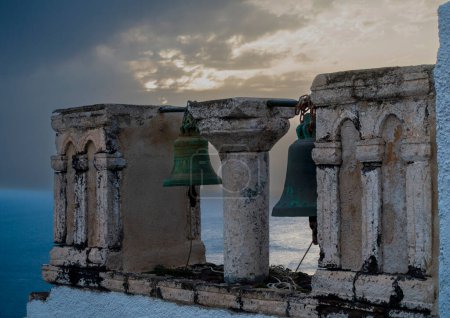Foto de Las campanas erosionadas de un monasterio griego dan al mar Egeo mientras se pone el sol, creando una escena serena e histórica. - Imagen libre de derechos