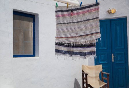 Photo for A handwoven textile hangs to dry on a white wall of a Greek home, next to a blue door, capturing the essence of island life. - Royalty Free Image