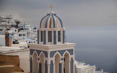 Foto de La distinguida cúpula azul de una iglesia de Santorini destaca sobre el dramático telón de fondo de una tormenta inminente. - Imagen libre de derechos