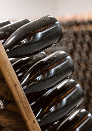 Großaufnahme staubbedeckter Weinflaschen auf Holzregalen, die anmutig in einem dunklen Keller altern.