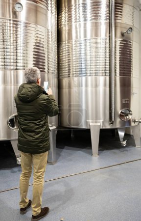 Photo for A winemaker checks the wine fermentation tanks, ensuring quality in the winemaking process. - Royalty Free Image
