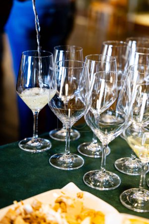 White wine being poured into a row of fine glasses, set up for a professional wine tasting event.