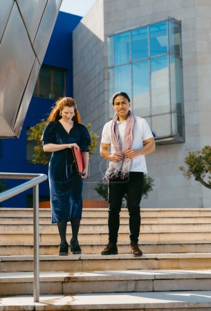 A creative duo descends a flight of stairs, each showcasing their individual style against the backdrop of a modern building.