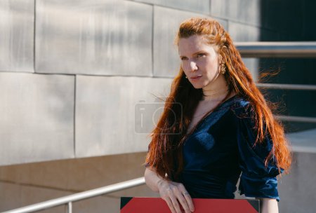 A red-haired woman in a velvet dress leans on a railing, her confident gaze enhancing the urban elegance.