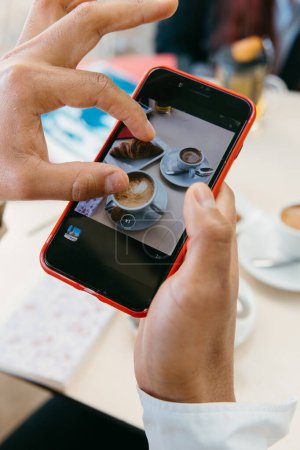 Foto de Las manos enmarcan un elegante diseño de taza de café en un teléfono inteligente, personificando la cultura moderna de las redes sociales. - Imagen libre de derechos