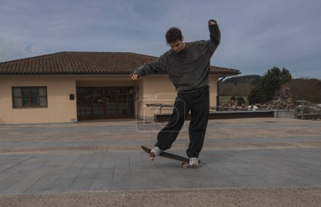 A focused skateboarder perfects his balancing technique on his board in an expansive urban plaza, under an overcast sky.