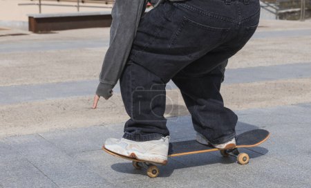 Téléchargez les photos : Un gros plan détaillé mettant en valeur le jeu de jambes d'un skateboarder pendant qu'il roule, mettant en valeur le style et la technique essentiels au skateboard. - en image libre de droit