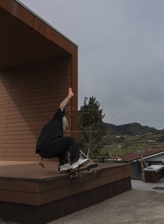 Téléchargez les photos : Capturé au milieu du tour, un skateboarder saute du bord d'une structure architecturale avec un paysage rural derrière lui. - en image libre de droit