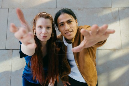 Téléchargez les photos : Couple souriant étendant les mains vers la caméra avec un geste amical. - en image libre de droit