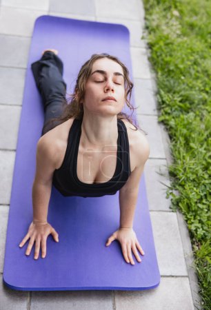 Photo for Fitness enthusiast enjoys a calming Cobra pose on a yoga mat in a serene garden setting." - Royalty Free Image