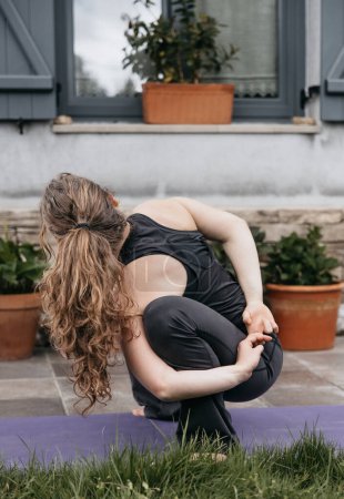 A young woman transitions between yoga poses, demonstrating focus and flexibility in her home garden yoga practice