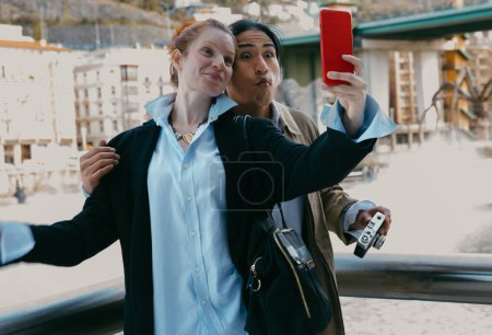 A young mixed-race couple enjoys a playful moment taking a selfie on an urban bridge, showcasing their joy and diversity.