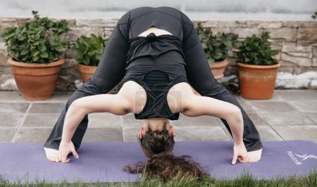 Téléchargez les photos : Une femme effectue une pose de yoga sur un tapis dans un cadre de jardin serein. - en image libre de droit