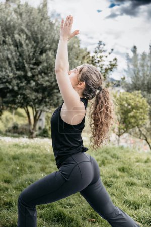 Téléchargez les photos : Une femme concentrée s'engage dans une posture de yoga dans un parc ensoleillé avec une végétation luxuriante. - en image libre de droit