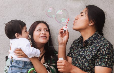Eine ecuadorianische Familie mit einem Vater mit traditionellem Zopf genießt einen verspielten Moment mit Seifenblasen und ihrem Baby.