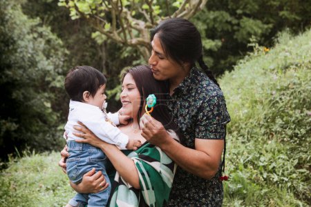 Téléchargez les photos : Une famille équatorienne profite d'un moment serein dans le jardin, avec un père portant une tresse traditionnelle et sa femme tenant leur bébé. - en image libre de droit