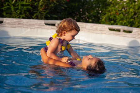 Foto de Two young sisters share a tender moment in the swimming pool, showcasing their bond and love during a playful water activity. - Imagen libre de derechos
