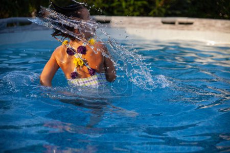 Photo for Captured mid-motion, a young girl creates a dynamic splash by flipping her hair while swimming in a pool, illustrating a lively summer moment. - Royalty Free Image