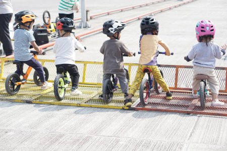 Téléchargez les photos : Enfants de 2 à 5 ans prêts à courir sur un vélo d'équilibre au point de départ dans une aire de stationnement, vue arrière, derrière la vue prise de vue. - en image libre de droit